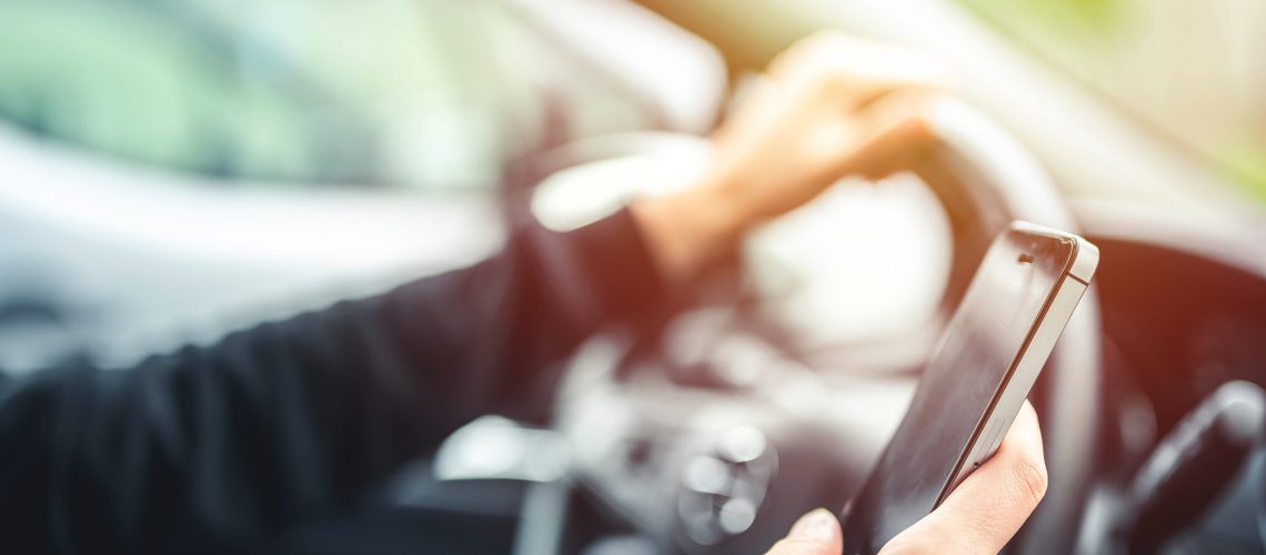 Woman looking at mobile phone while driving a car. Transportation and vehicle concept.